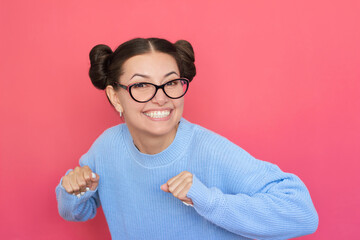 Young happy pretty Caucasian woman wearing blue sweater and wearing glasses dancing with happiness,...