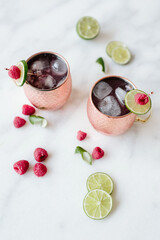 Two cocktails in copper mugs with lime and raspberry