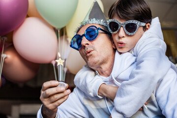 father and son in party glasses are blowing out birthday candle