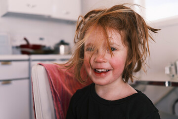 Happy young child with messy hair smiling in kitchen