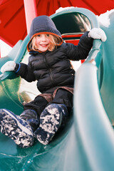 Happy child playing on slide in snowy playground