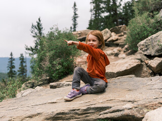 Child sitting on a rock pointing in the distance during a hike