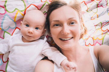Portrait of mother and baby, top view. Smiling mom takes selfie of herself and her cute little baby...