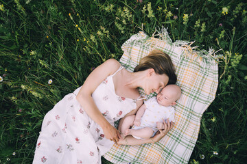 Smiling mom and baby lying on blanket on green grass at summer. Family relaxing and having picnic...