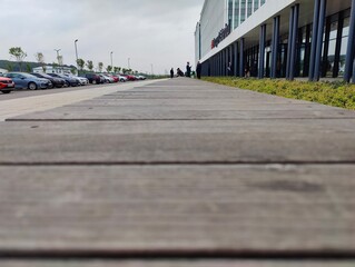 Obraz premium Wooden Boardwalk with Well-Maintained Planks in a Pedestrian-Friendly Outdoor Setting Adjacent to Parking Area
