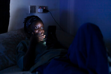 Young African Woman in Dark Room Illuminated by Mobile Phone Light, Highlighting Digital Addiction