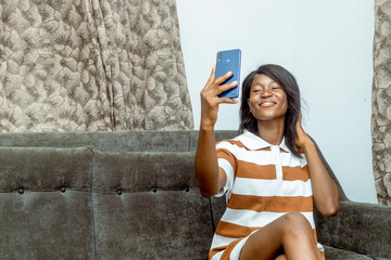 Young African Woman Engaging with Smartphone While Relaxing on Sofa