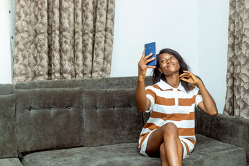 Young African Woman Engaging with Smartphone While Relaxing on Sofa