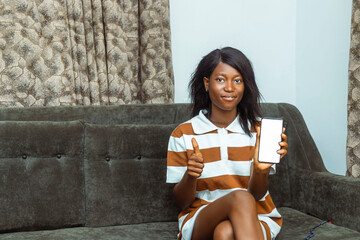 Young African woman sitting on a sofa, smiling and holding a smartphone.