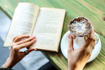 Person Reading Book and Holding Pastry at Outdoor Cafe