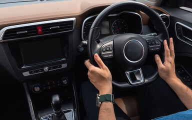 Hands hold the steering wheel inside the car. A man hands holding steering wheel while driving car.