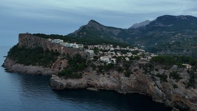 Drone shot of the coastal buildings on a sea cliff in Port de Soller village at sunset, Spain