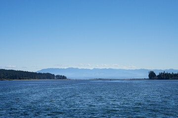 Looking over the  ocean water towards a distant spit, with light paths made by boat wakes.