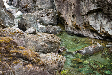 A beautiful small creek rushing between steep colorful rocks to a bright green pool of water.