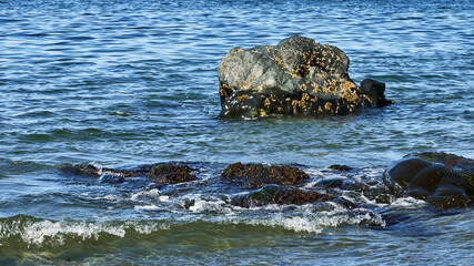 View of rocks with small waves splashing against the front rocks and a rock with barnacles.