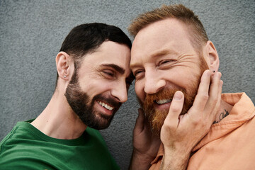 Two men in love smile and pose for a portrait against a grey wall, radiating happiness and...