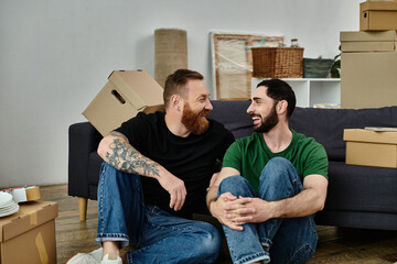 A gay couple, in love, sit atop a couch surrounded by moving boxes, starting a new life together.