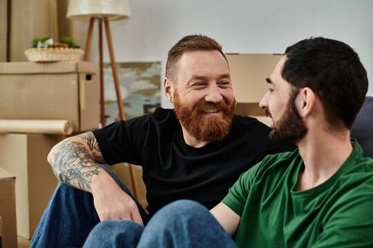 Two men, part of a gay couple in love, relax on a couch in their new home surrounded by moving boxes.