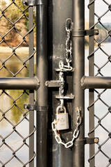 Closeup vertical shot of a lock on a chain link gate with the ocean in the background on a sunny day