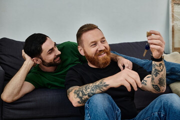 A gay couple relaxes atop a couch in their new home, taking a moment together, looking at key
