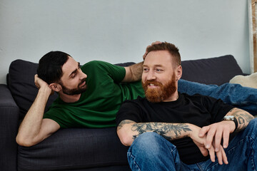 A gay couple shares a tender moment as they sit closely on top of a couch, surrounded by moving...