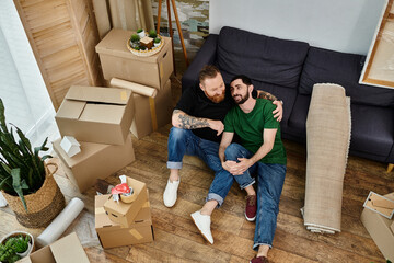 A gay couple sits atop a wooden floor, contemplating their new life together as they move into...