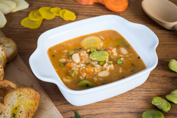 Aguadito de pollo is a traditional Peruvian soup prepared with chicken, aji amarillo peppers, peas, corn, onions, potatoes, rice, and cilantro closeup on the bowl on the wooden table. Vertical