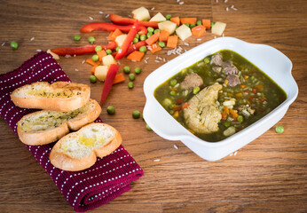Aguadito de pollo is a traditional Peruvian soup prepared with chicken, aji amarillo peppers, peas, corn, onions, potatoes, rice, and cilantro closeup on the bowl on the wooden table. Vertical