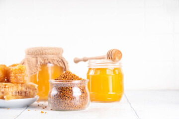 Bee pollen jar and spoon with honey and honeycomb. Trendy superfood, antioxidant organic powder, on white table background copy space
