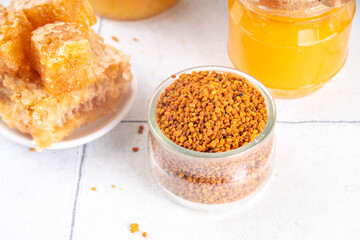 Bee pollen jar and spoon with honey and honeycomb. Trendy superfood, antioxidant organic powder, on white table background copy space