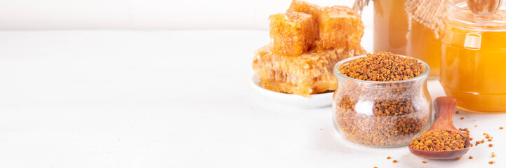 Bee pollen jar and spoon with honey and honeycomb. Trendy superfood, antioxidant organic powder, on white table background copy space