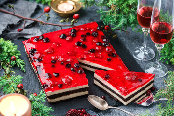 Layer creamy mousse cake with berry jelly on grey background with glasses of wine, berries, candles...