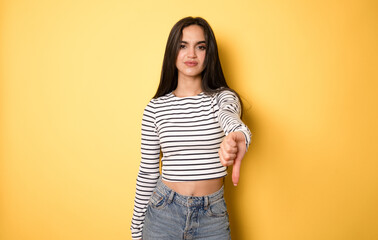 Young beautiful girl wearing striped shirt standing over isolated yellow background looking unhappy...