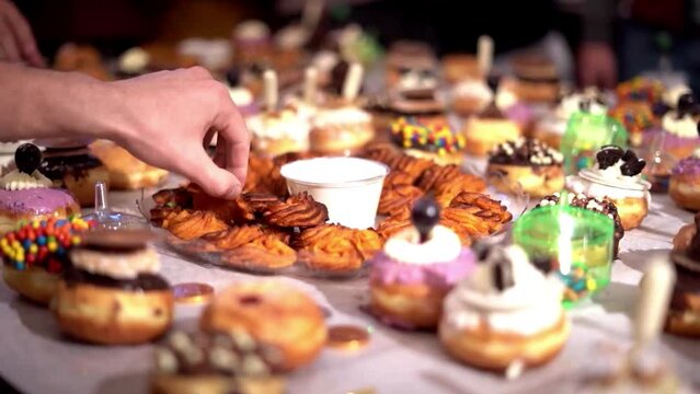 Close-up slow mo shot of a hand picking up an Indian dessert from a table full of food.