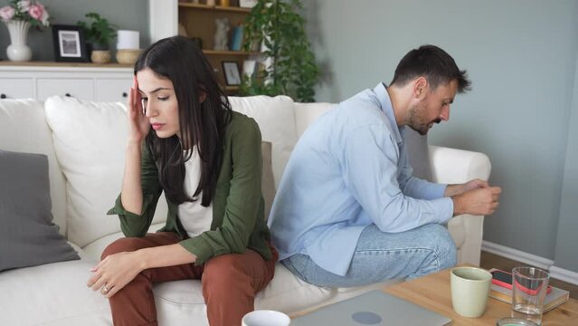 Young couple having relationship difficulties and arguing at home. Two people man and woman sitting on sofa, not talking after argue, feeling depressed and insulted, not talking.