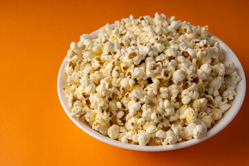 White bowl of popcorn on an orange table.