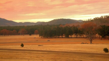 Obraz premium A field with trees, mountains, pink sky, orange background