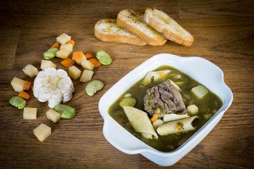 A bowl of Peruvian menestron soup. With chunks of meat, noodles, chopped carrots, corn and coriander to give it the green color.