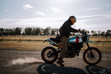 a man standing in the middle of a dirt road on a motorcycle