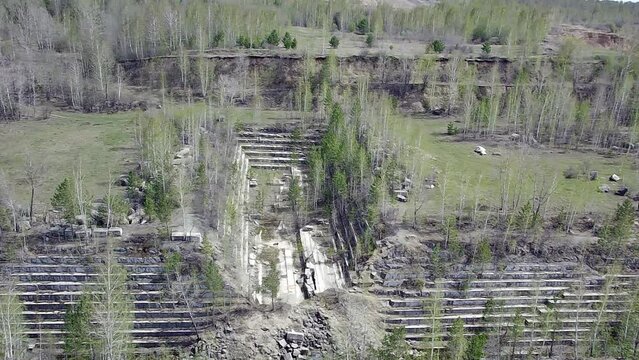 An old and abandoned marble quarry looking like giant steps in the shape of a "T" beech tree, in many places overgrown with young trees on a sunny spring day. A huge clearing surrounded by mixed fores