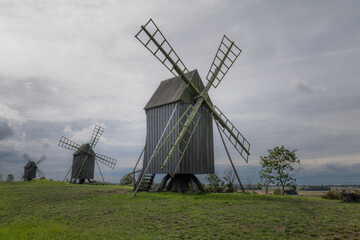 Old windmills in a grassy field under cloudy skies