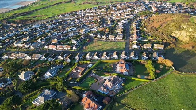 Drone over Deganwy, north Wales on sunny afternoon, revealing lush green fields, houses and sea