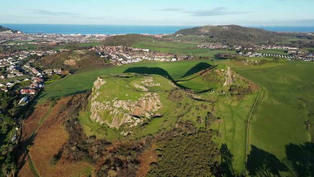 Drone of ancient volcanic butte in Deganwy, north Wales with green fields, houses and blue sea