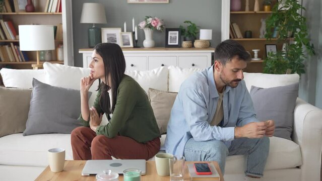 Young couple having relationship difficulties and arguing at home. Two people man and woman sitting on sofa, not talking after argue, feeling depressed and insulted, not talking.