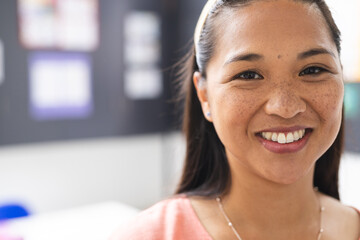 A young biracial female teacher in classroom smiles at camera with copy space - Powered by Adobe