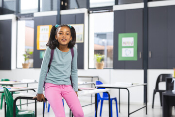 In school, young African American girl standing by a desk in a classroom with copy space
