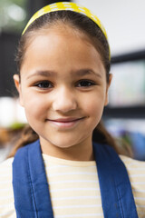 In school, in classroom, biracial young girl wearing a blue vest, smiling