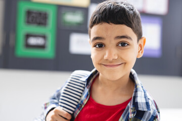 In school, young biracial boy with a striped backpack is smiling in the classroom - Powered by Adobe