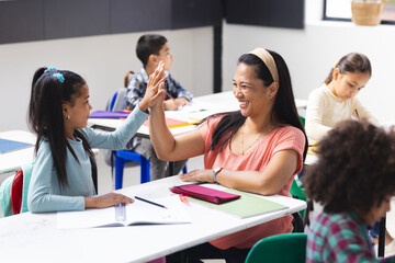 Biracial teacher high-fiving daughter in classroom, other students watch