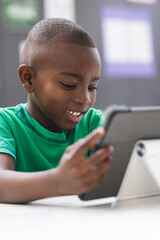 In school, young African American boy is focusing on a tablet in the classroom